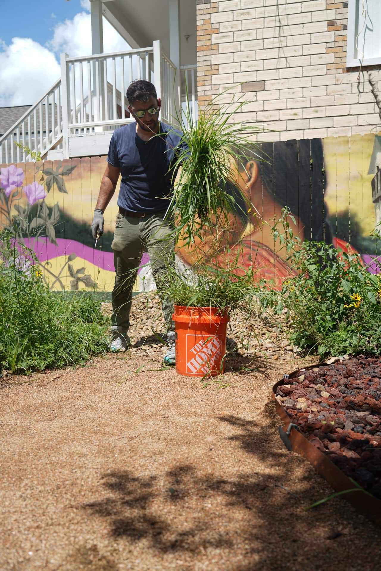 A neighbor carrying a bucket of pulled weeds along the mural path
