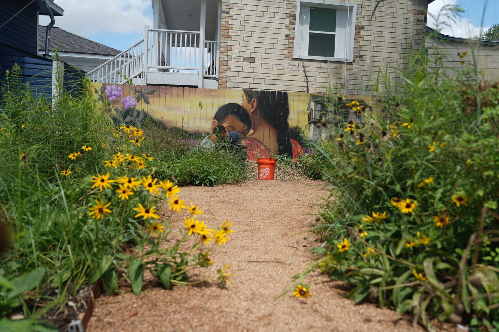 A neighbor pulling weeds in front of the painted mural, soil bags stacked behind